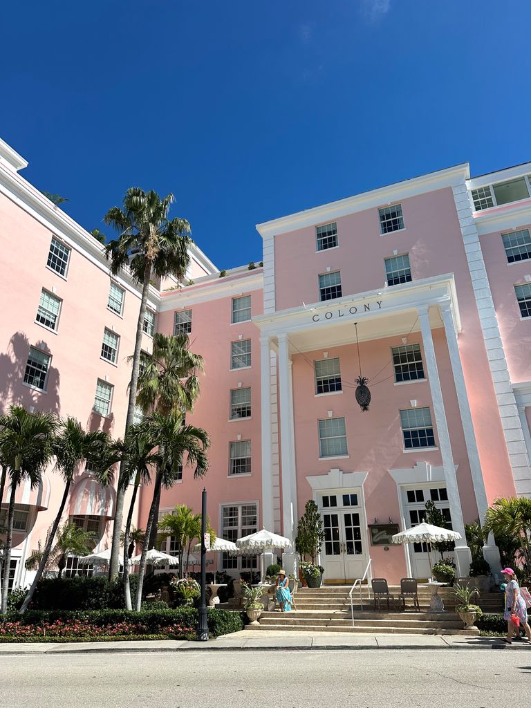Charming pink colonial-style hotel facade with beautiful palm trees on a sunny day.