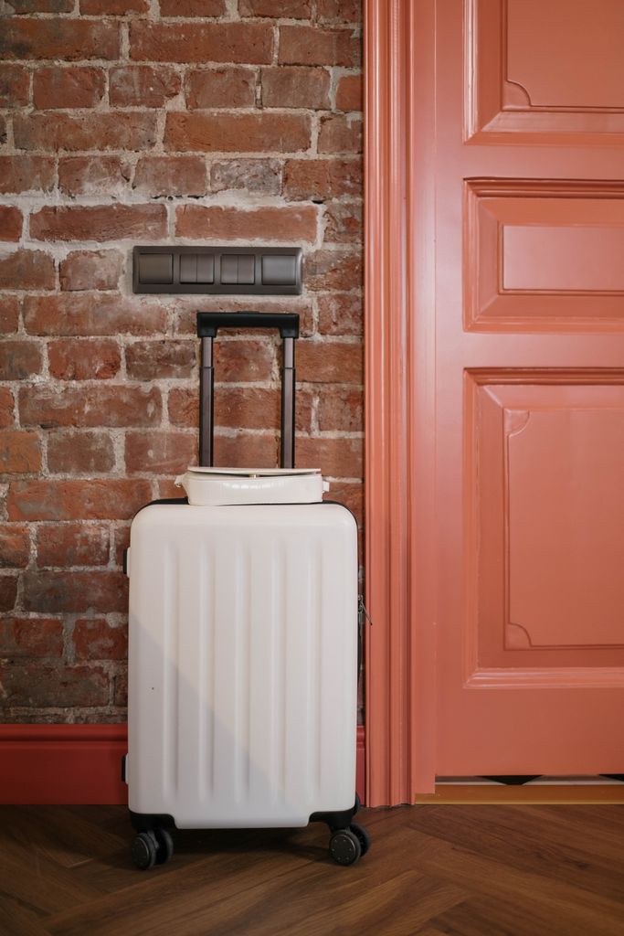 Compact white suitcase against a rustic brick wall beside a coral door, perfect for travel themes.