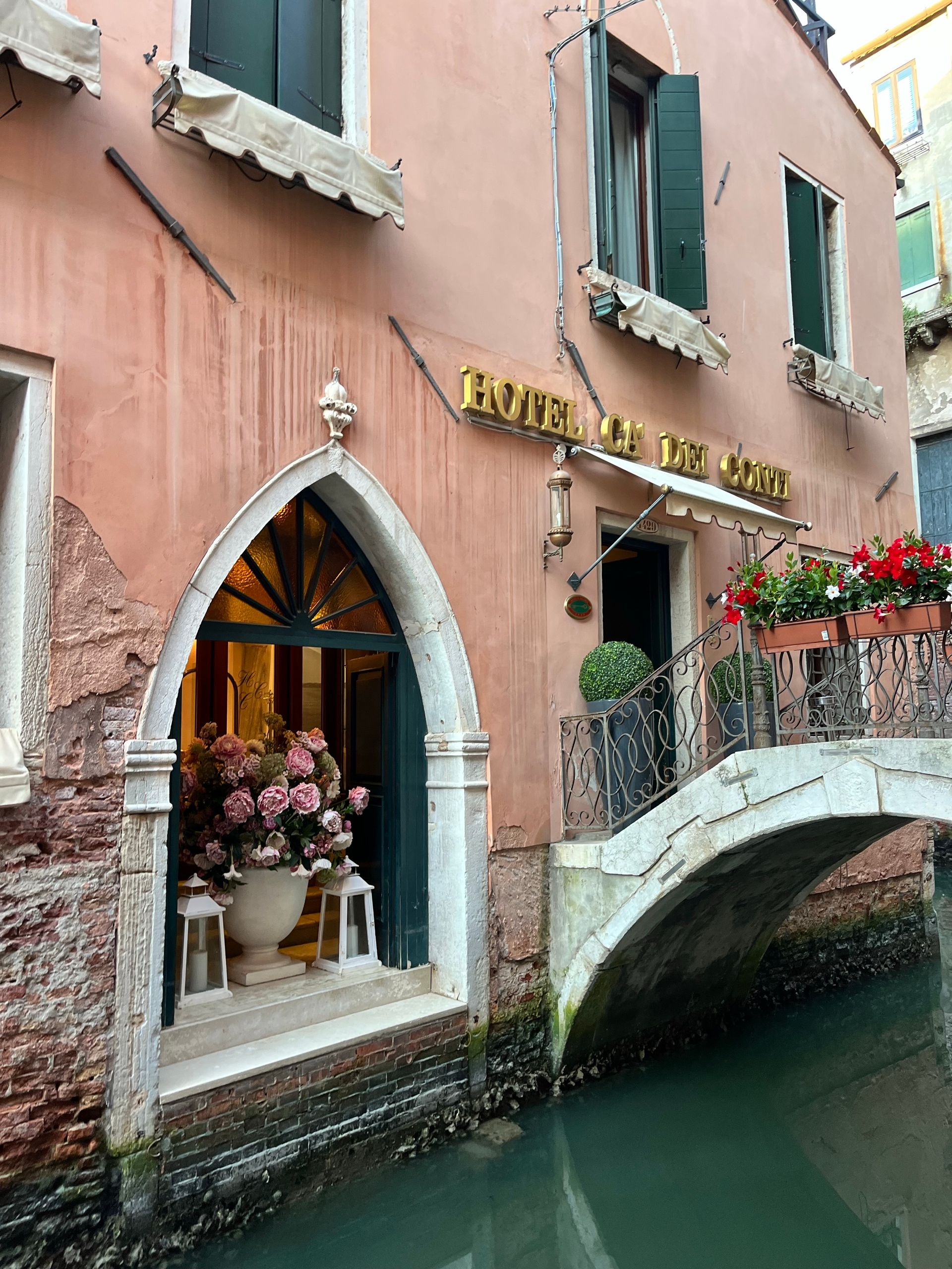 Elegant entrance of a Venetian hotel by a serene canal with flowers.