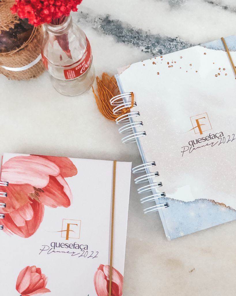 Flat lay of trendy 2022 planners with floral designs and a Coca-Cola bottle on a marble background.